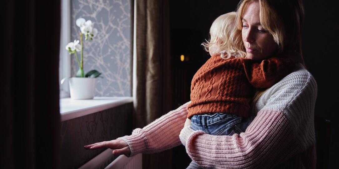 Mother With Son Trying To Keep Warm By Radiator At Home During Cost Of Living Energy Crisis Mother With Son Trying To Keep Warm By Radiator At Home During Cost Of Living Energy Crisis